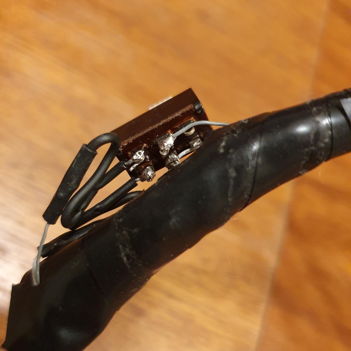 The modified cable with a small slide switch sitting on top of it, seen from below to show the wires soldered to four pins of the switch.